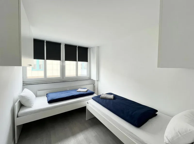 Zweibettzimmer mit dunkelblauer Bettwäsche und großem Fenster